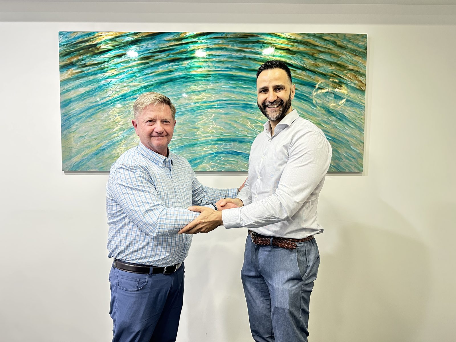 Dr Peter Barry shaking hands with Dr Zaid Al Momani in front of an aqua-toned water artwork at Aqua Dental, Paradise Point